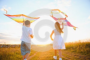 Brother and sister playing with kite and plane at the field on the sunset.