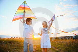 Brother and sister playing with kite and plane at the field on the sunset.