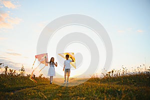 Brother and sister playing with kite and plane at the field on the sunset.