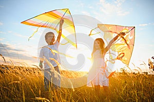 Brother and sister playing with kite and plane at the field on the sunset.