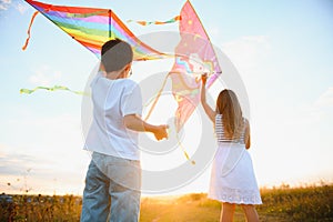 Brother and sister playing with kite and plane at the field on the sunset.