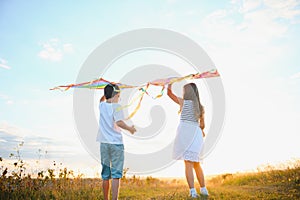 Brother and sister playing with kite and plane at the field on the sunset.