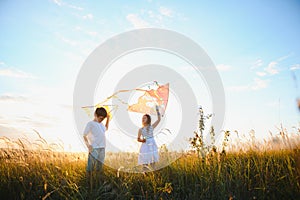 Brother and sister playing with kite and plane at the field on the sunset.