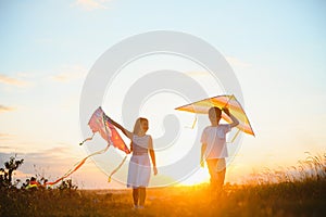 Brother and sister playing with kite and plane at the field on the sunset.