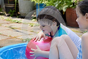 brother and sister playing with a large colorful rubber ball in a shallow swimming pool in the backyard