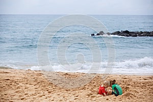 Brother and sister playing with sand and water on a tropical beach, dressed in protective wetsuit