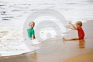 Brother and sister playing with sand and water on a tropical beach, dressed in protective wetsuit