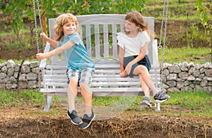 Brother and sister playing, swinging on swing in spring park outdoors. Little boy and girl kids enjoying spring. Kids