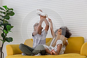 Brother and sister playing togetherness fun in living room, Two little kids siblings seated on sofa holding airplane toy and book