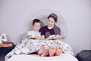 Brother and sister read a book together and laugh. Happy and joyful children with bare feet on the bed. The legs are covered with