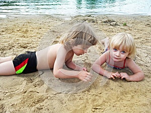 Brother and sister relaxing on sand near lake