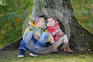 Brother and sister seated against a tree