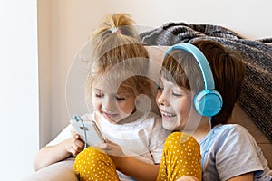 Brother and sister sit at home on the couch with smartphones, girl in headphones, concept kids and modern technology