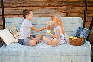 Brother and sister sit opposite each other on a garden swing and eat green apples. Beautiful happy caucasian children in the