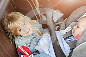 Brother and sister sitting in car in safety seat. Siblings on passenger places having fun together during travel by