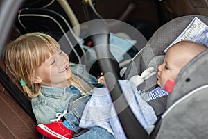 Brother and sister sitting in car in safety seat. Siblings on passenger places having fun together during travel by