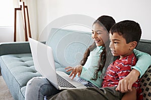 Brother And Sister Sitting On Sofa At Home Having Fun Playing On Laptop Together