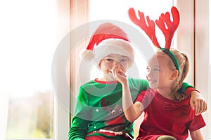 Brother and sister sitting on window sill at christmas time, having fun together. Christmas family time lifestyle.