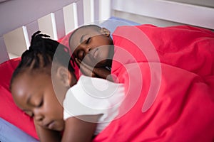 Brother and sister sleeping on bed at home