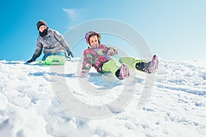 Brother and sister slide down from the snow slope. Winter time p