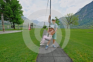 Brother with sister swinging in playground at Hallstatt, Austria