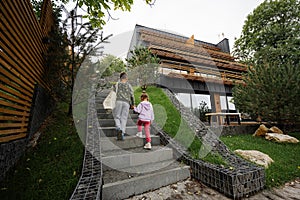 Brother with sister walking on stairs against modern wood stone house