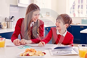 Brother And Sister Wearing School Uniform Doing Homework On Kitchen Counter With Healthy Snacks