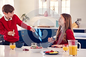 Brother And Sister Wearing School Uniform In Kitchen Have Fun Hanging Spoon From Nose At Breakfast