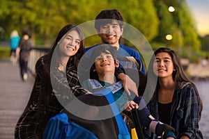 Brother and sisters surrounding disabled boy in wheelchair at park