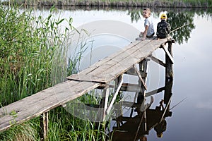 Brothers fishing on the river bank. Kids siting with sticks in hands.