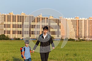 Brothers go to school. The teenager and his younger brother with backpacks hold hands, brothers smile happy faces of