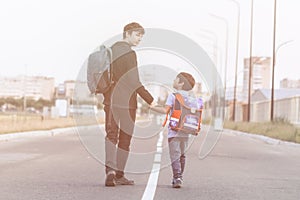 Brothers go to school. The teenager and his younger brother with backpacks hold hands  brothers smile happy faces of children.