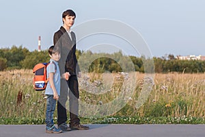 Brothers go to school. The teenager and his younger brother with backpacks hold hands, brothers smile happy faces of children.