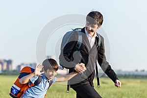 Brothers go to school. The teenager and his younger brother with backpacks hold hands, brothers smile happy faces of children.