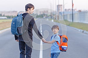 Brothers go to school. The teenager and his younger brother with backpacks hold hands, brothers smile happy faces of children.