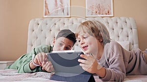 Brothers with tablet computer in light room. Children, boys playing games on tablet computer, emotions. Daytime. Playing