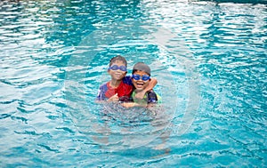 Brothers wear a swimsuit and goggles. Smile and enjoy playing in the water in the blue pool