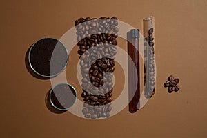 On brown background, lab glassware container coffee beans, grounds and liquid decorated. Shape of cosmetic tube arranged by