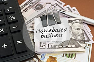 On a brown background lies a calculator and dollars on a clip with an inscription on paper - Homebased business