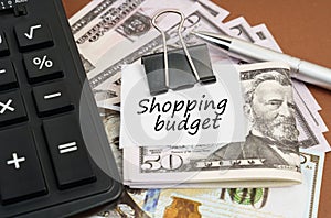 On a brown background lies a calculator and dollars on a clip with an inscription on paper - Shopping budget