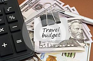 On a brown background lies a calculator and dollars on a clip with an inscription on paper - Travel budget