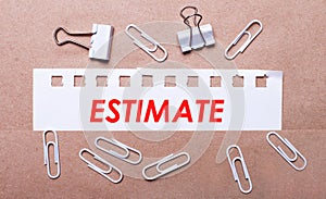 On a brown background, white paper clips and a torn strip of white paper with the text ESTIMATE