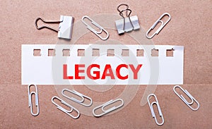 On a brown background, white paper clips and a torn strip of white paper with the text LEGACY