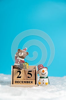 Brown bear wearing a Christmas hat and snowman sitting on wooden block calendar set on the Christmas date 25 december on white woo