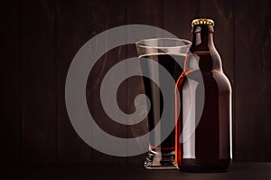 Brown beer bottle belgian steinie and glass pilsner with porter on dark wood board, copy space, mock up.