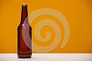 Brown beer bottle with drops of condensate on yellow background