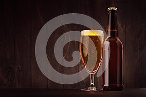 Brown beer bottle and glass tulip with golden lager on dark wood board, copy space, mock up.