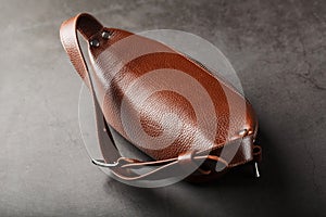 A brown belt bag made of textured brown leather on a black stone background. Elegant fanny pack brown bag with a zipper