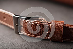 A brown belt bag made of textured brown leather on a black stone background. Elegant fanny pack brown bag with a zipper