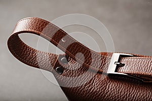 A brown belt bag made of textured brown leather on a black stone background. Elegant fanny pack brown bag with a zipper